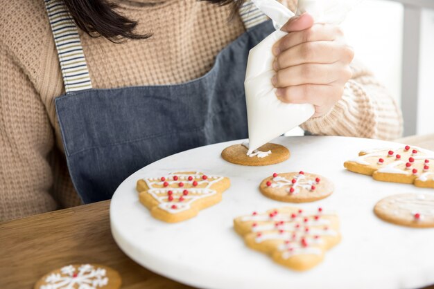 Mujer joven que adorna las galletas de la Navidad del pan de jengibre con la formación de hielo real