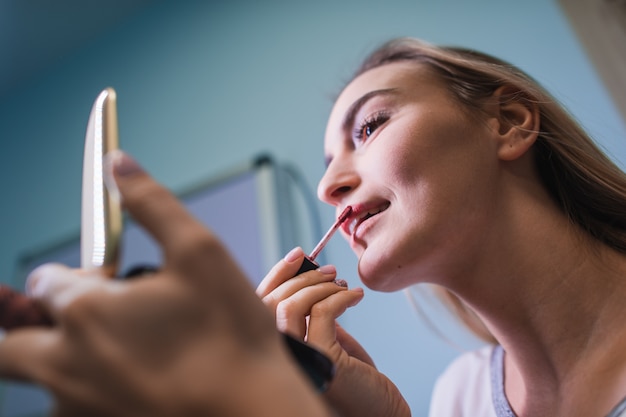 Mujer joven que aplica el lápiz labial que mira el espejo