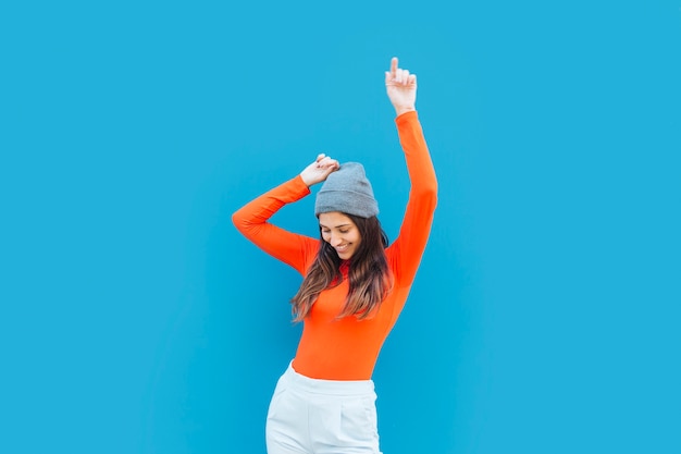 Mujer joven que baila con el brazo levantado delante de fondo azul