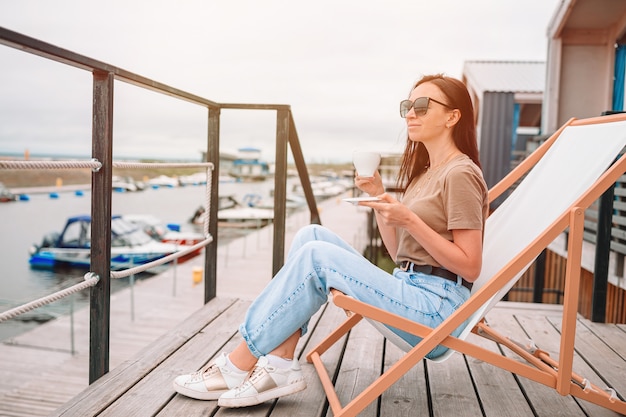 Mujer joven que bebe el café caliente que disfruta de vista de la playa.