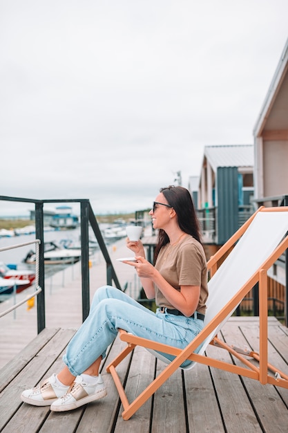 Mujer joven que bebe el café caliente que disfruta de vista de la playa.