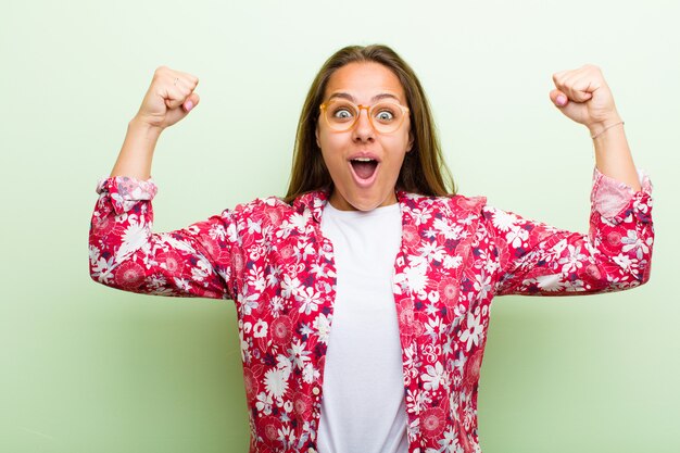 Mujer joven que celebra un éxito increíble como una ganadora, luciendo emocionada y feliz diciendo: ¡Toma eso! sobre pared verde