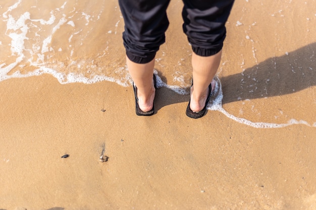 Mujer joven que se coloca en la playa con la onda sobre sus pies