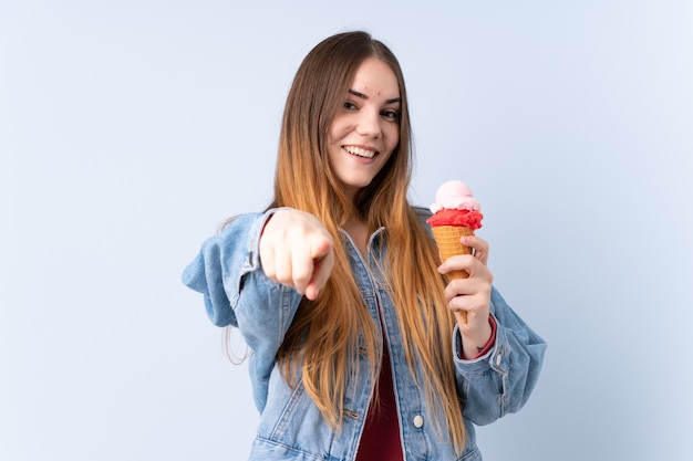 Mujer joven que come el helado sobre la pared aislada