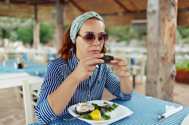 Foto mujer joven que come la ostra en un restaurante al aire libre