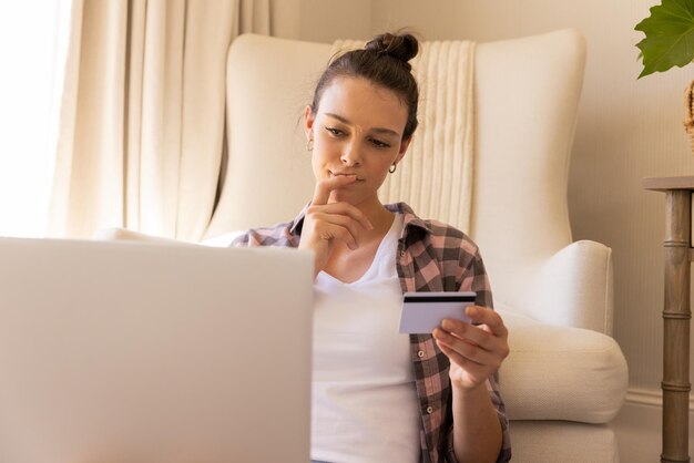 Mujer joven que compra en línea con tarjeta de crédito y usa una computadora portátil en el espacio de copia de casa