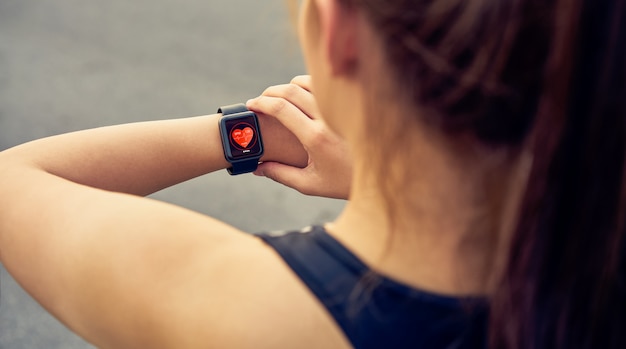 Mujer joven que controla el reloj deportivo que mide la frecuencia cardíaca y el rendimiento después de correr.