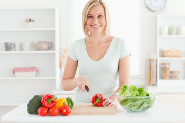 Foto la mujer joven que corta verduras sonríe en cámara