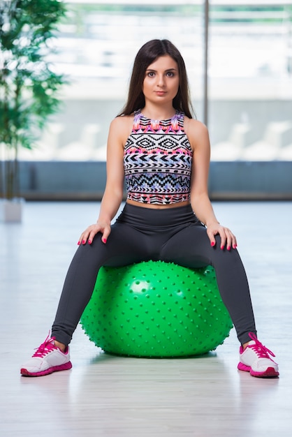 Foto mujer joven que ejercita con la bola suiza en concepto de la salud