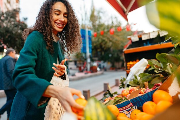 Mujer joven que elige los productos que va a comprar en el puesto del mercado agrícola local
