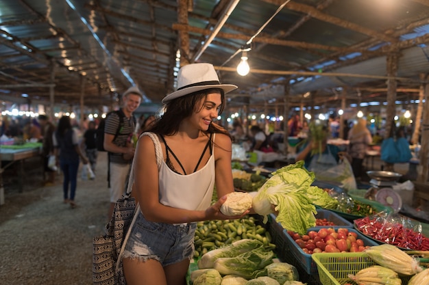 Mujer joven que elige verduras en compras de la muchacha del mercado en bazar de la calle