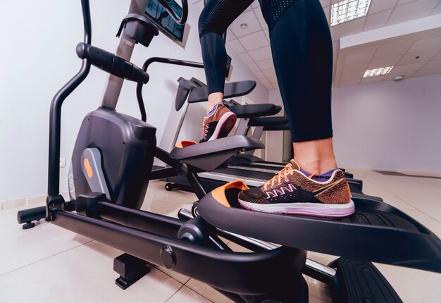 Mujer joven que entrena en el entrenador cruzado en el gimnasio.