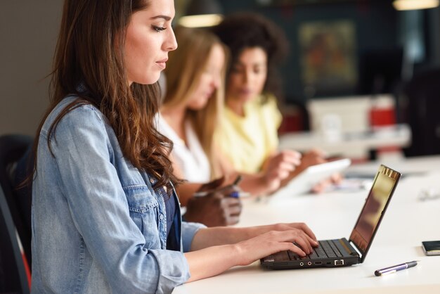 Mujer joven que estudia con la computadora portátil en el escritorio blanco.