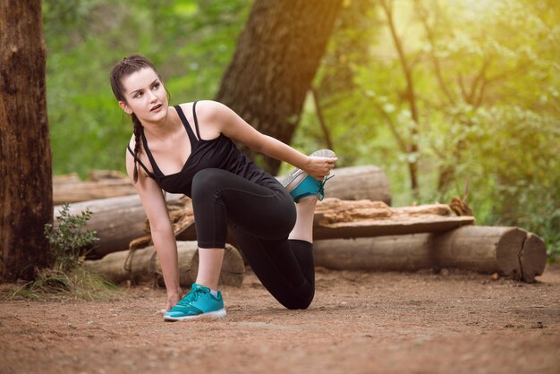 Mujer joven que se extiende antes de correr en el área boscosa del bosque Entrenamiento y ejercicio para Trail Run Marathon Endurance Fitness Concepto de estilo de vida saludable