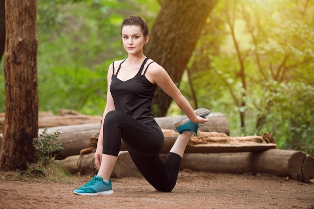 Mujer joven que se extiende antes de correr en el área boscosa del bosque Entrenamiento y ejercicio para Trail Run Marathon Endurance Fitness Concepto de estilo de vida saludable
