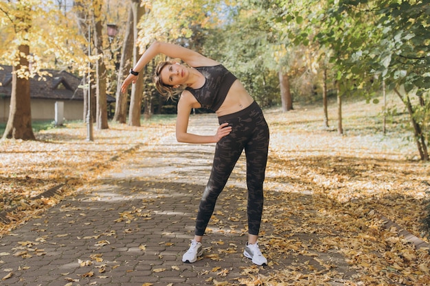 Mujer joven que se extiende en el parque soleado. Chica fitness entrenamiento al aire libre en el paisaje de la naturaleza