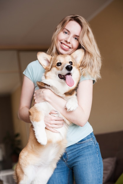 Mujer joven que guarda el perrito del corgi galés cerca de su cara. Welsh Corgi Pembroke cachorro, corte feliz