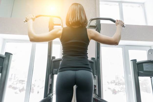 Mujer joven que hace los ejercicios para la parte posterior en la máquina de la aptitud en gimnasio