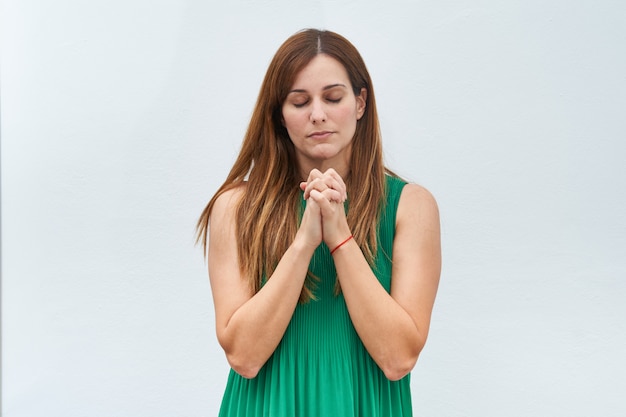 Mujer joven que hace el gesto de rezar en un fondo blanco.