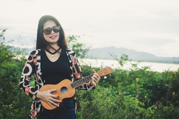 Mujer joven que juega en Ukulele marrón en el parque.