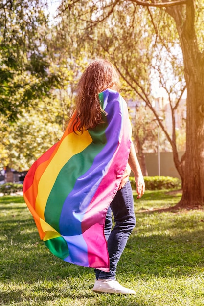 Mujer joven que lleva una bandera del arco iris LGBTQ como capa para el mes del orgullo y la diversidad del amor de celebración