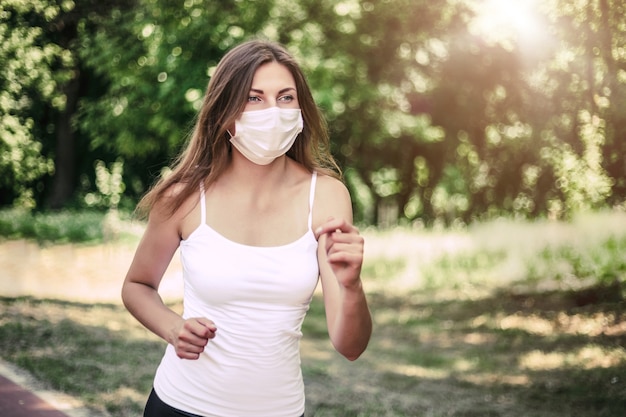 Una mujer joven que lleva una máscara respiratoria protectora corre por el parque soleado y mira el espacio de la copia, cuarentena, covid-19