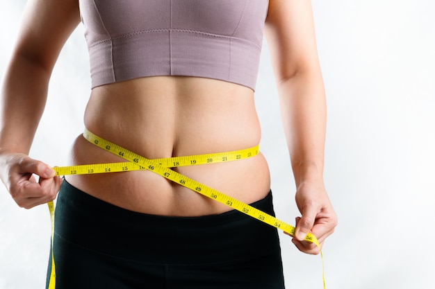 Mujer joven que mide su cintura gorda excesiva del vientre con cinta métrica, concepto de estilo de vida dieta mujer