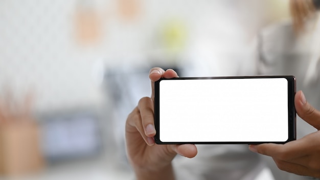 La mujer joven que muestra la pantalla vacía del teléfono inteligente.