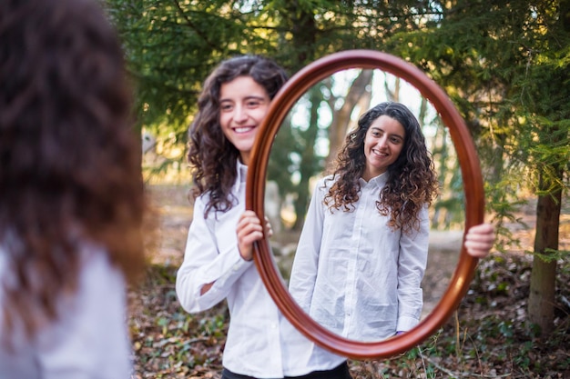 Mujer joven que muestra el reflejo de la hermana gemela en el bosque