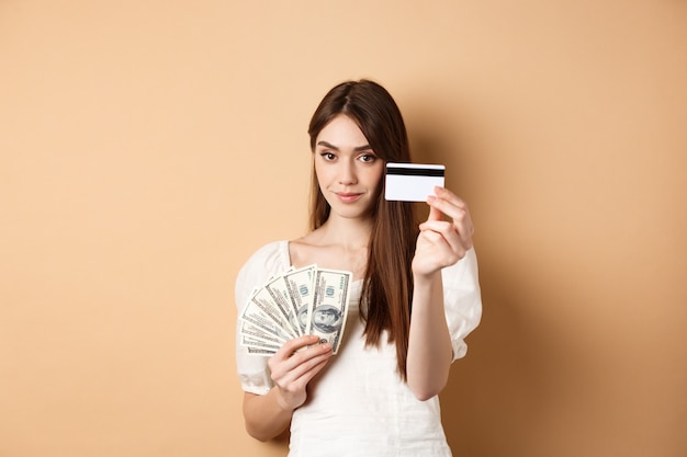 La mujer joven que muestra la tarjeta de crédito plástica prefiere el pago sin contacto en lugar de los billetes de dólar de pie ...