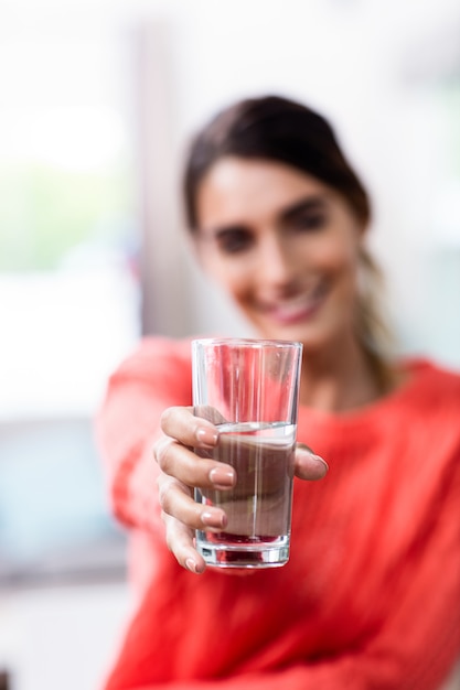 Mujer joven que muestra el vaso con agua