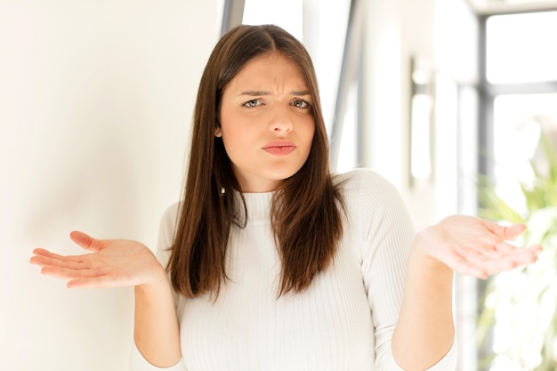 Mujer joven que parece desconcertado, confundido y estresado preguntándose entre diferentes opciones sintiéndose inseguro