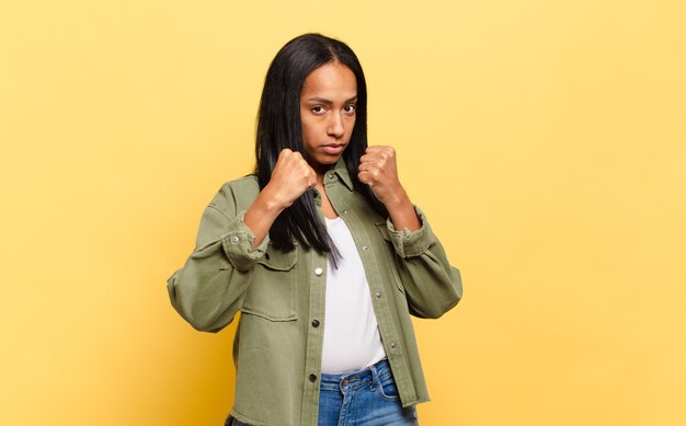 Mujer joven que parece segura, enojada, fuerte y agresiva, con los puños listos para pelear en posición de boxeo