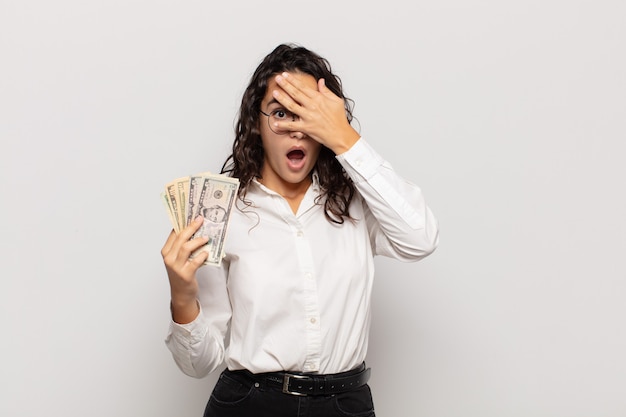 Foto mujer joven que parece sorprendida, asustada o aterrorizada, cubriendo la cara con la mano y mirando entre los dedos