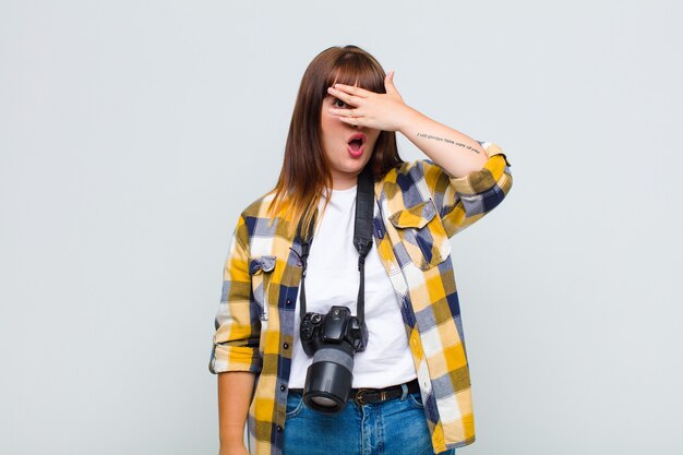 Mujer joven que parece sorprendida, asustada o aterrorizada, cubriendo la cara con la mano y mirando entre los dedos