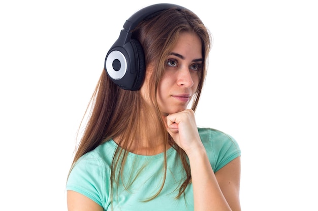 Mujer joven que se pregunta con camiseta azul escuchando música con auriculares negros en el estudio