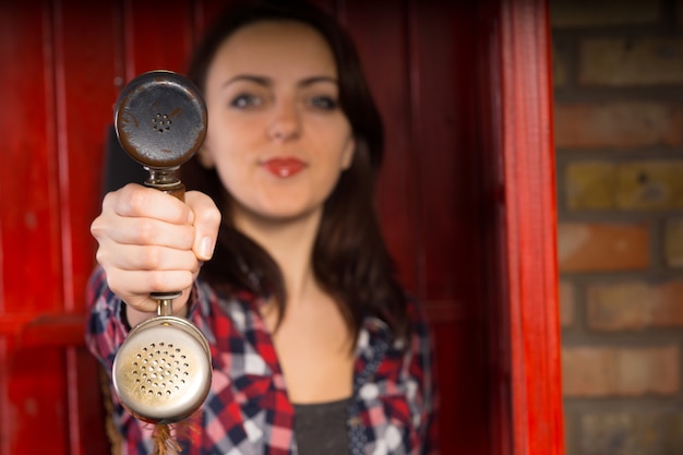 Mujer joven que presenta un auricular de teléfono al espectador en su mano extendida con foco en el receptor