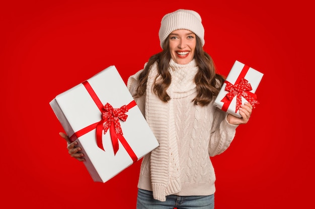 Mujer joven que presenta cajas envueltas en Navidad de pie sobre fondo rojo.