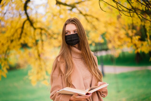 Mujer joven que se protege del virus de la corona al caminar en el parque. Fondo de otoño.