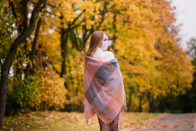 Una mujer joven que se protege del virus corona cuando camina en el parque. Fondo de otoño.