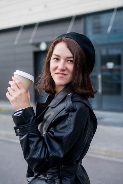 Mujer joven que se queda con teléfono inteligente y café frente a la oficina.