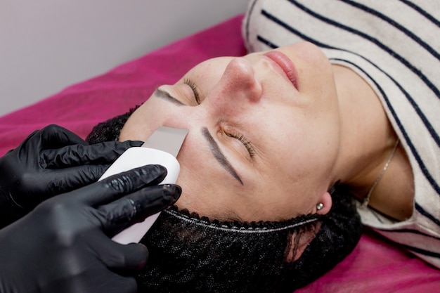 Mujer joven que recibe limpieza de peeling facial de cavitación por ultrasonido. Limpieza de tratamiento de cuidado de piel facial de cosmetología.