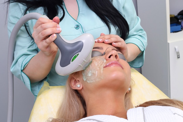 Foto mujer joven que recibe tratamiento de belleza facial, eliminación de la pigmentación en la clínica cosmética.