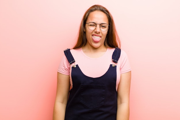 Mujer joven que se siente asqueada e irritada, sacando la lengua, no le gusta algo desagradable y asqueroso contra la pared rosa