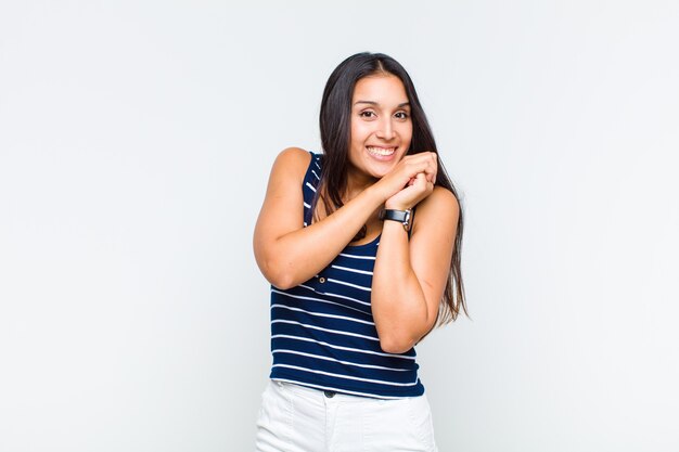 Mujer joven que se siente enamorada y se ve linda, adorable y feliz, sonriendo románticamente con las manos al lado de la cara