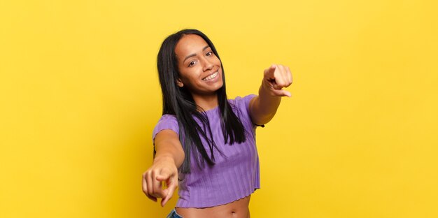 Mujer joven que se siente feliz y confiada, apuntando a la cámara con ambas manos y riendo, eligiéndote