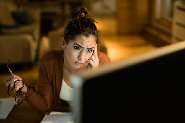 Mujer joven que se siente preocupada mientras usa la computadora y trabaja hasta tarde en casa