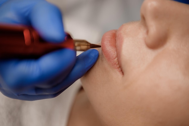 Mujer joven que se somete a un procedimiento de maquillaje de labios permanente en el primer plano del salón de tatuajes