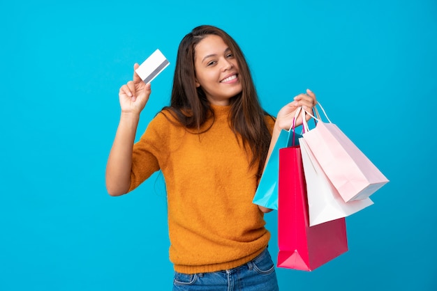 Mujer joven que sostiene bolsos de compras sobre la pared aislada