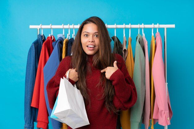 Mujer joven que sostiene bolsos de compras sobre la pared aislada